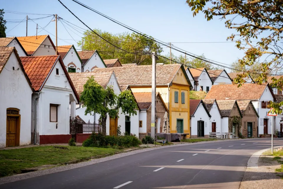 Csendes falusi utca fehérre meszelt présházak sorával, üres úttesttel.