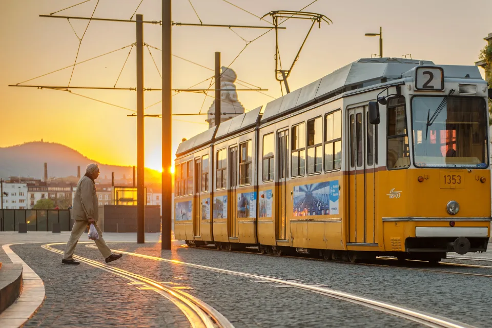 Villamos áll a belvárosi megállóban napnyugtakor, a síneken egy gyalogos sétál át.